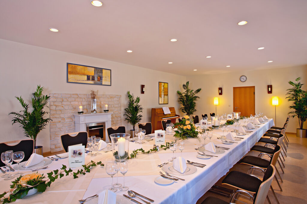 Festlich gedeckter Festsaal im Haus Silberbach mit langer Tafel, Kerzen, weißen Tischdecken, Blumenarrangements, Kamin und warmem Licht – Name Silberbach sichtbar