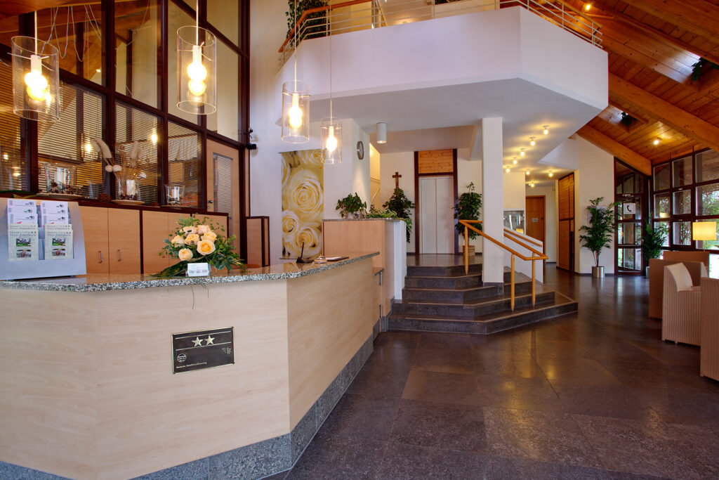 Rezeption im Hotel Haus Silberbach mit heller Holztheke, Granitkante, dekorativen Glaskronleuchten und Pflanzen im Hintergrund