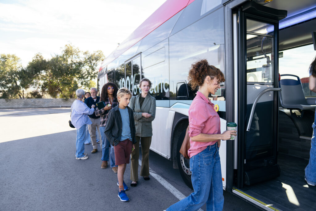 Gruppe von Reisenden wartet vor einem elektrischen Bus, mehrere Personen stehen Schlange, Bus zeigt 100% electric-Aufschrift, Outdoor-Szene in Oberfranken, Nähe Haus Silberbach